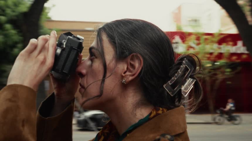 A woman captures a moment with her vintage analog camera as the city street life blurs behind her