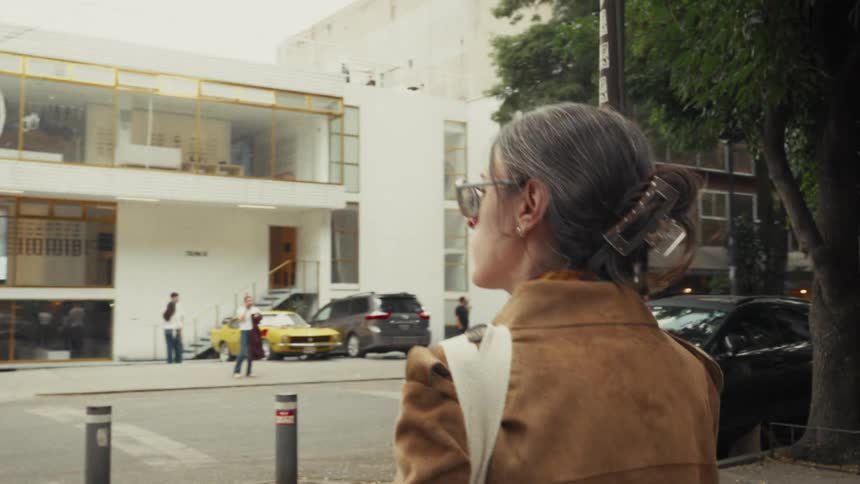 Over-the-shoulder slow-motion shot of a stylish woman walking down a city street, observing the urban architecture