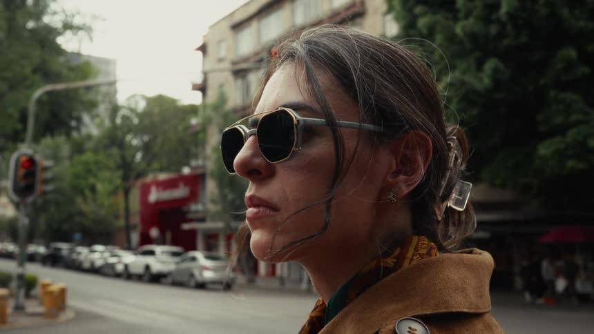 Close-up profile of a stylish woman in sunglasses with a serious expression waiting on a bustling city street