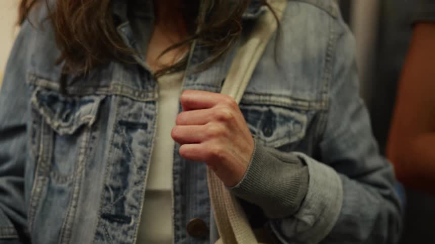 Close-up of a woman in a denim jacket holding the strap of her tote bag while riding on public transportation