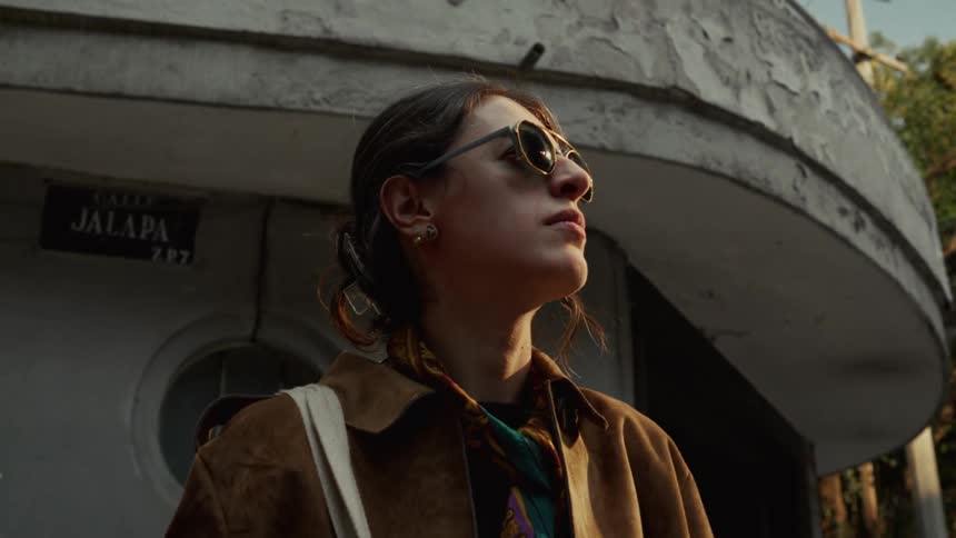 Low-angle shot of a fashionable woman standing in front of a building in the city, contemplating as the sun hits her face