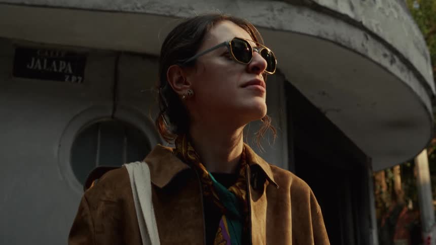 Cinematic low-angle close-up of a stylish woman with sunglasses standing in the city during golden hour