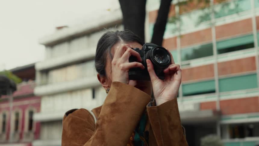 A female photographer focuses her vintage film camera while standing in a city square