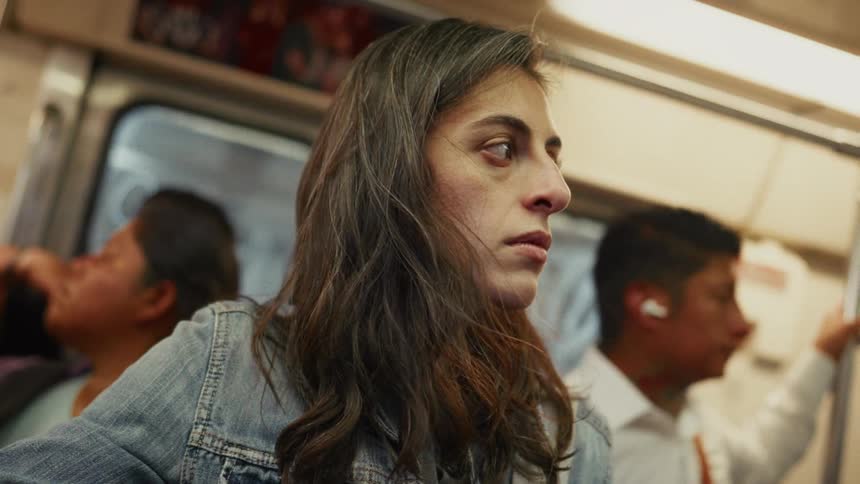 A weary woman with tired eyes rides a crowded subway car during her daily commute, lost in thought among other passengers