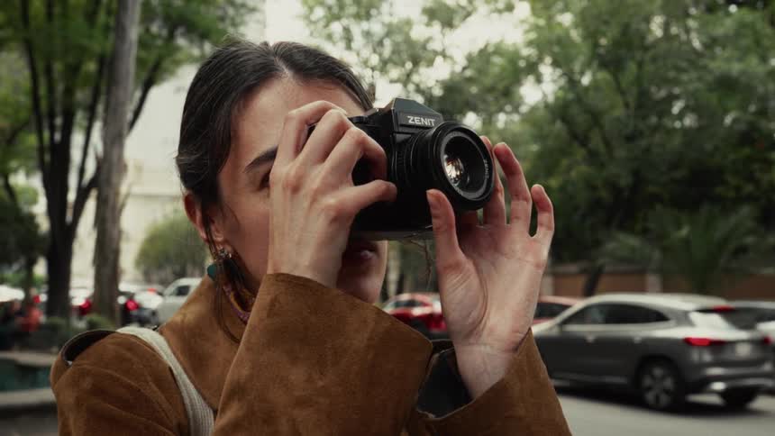 A young woman photographer adjusts the focus on her vintage film camera while taking a picture on a city street