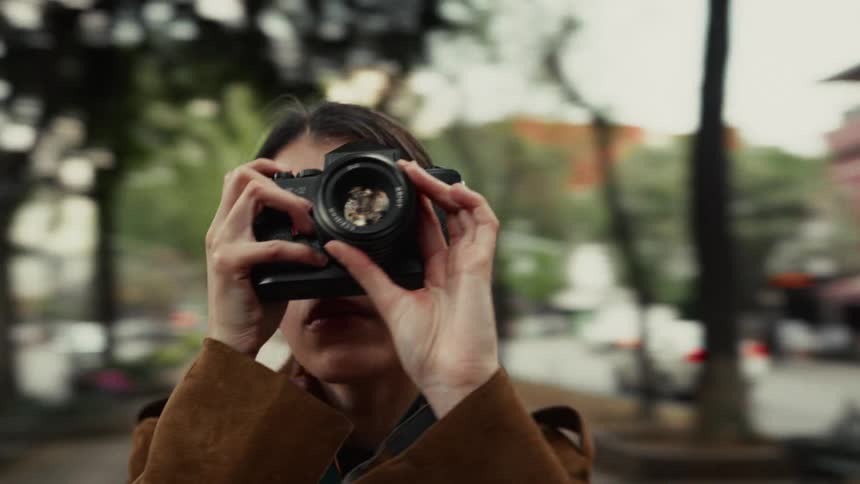 Dynamic orbital shot of a female photographer focusing her vintage film camera on a city street