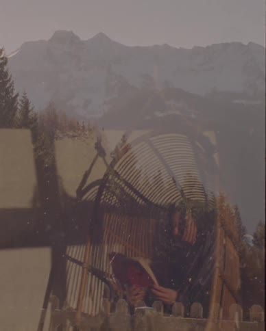 A vintage, dreamlike double exposure shows a person reading a book in a wicker chair with a snowy mountain range in the background