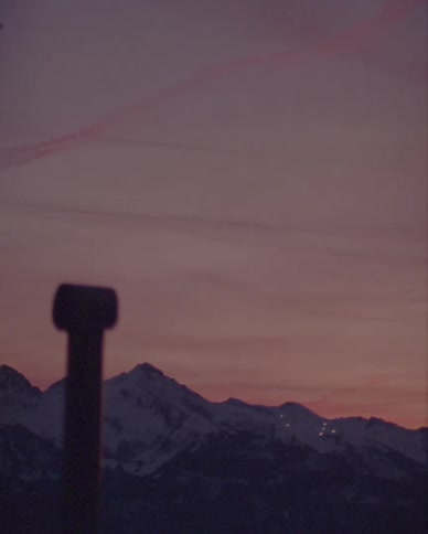 A vintage-style shot of a snow-capped mountain range under a purple and pink sunset sky