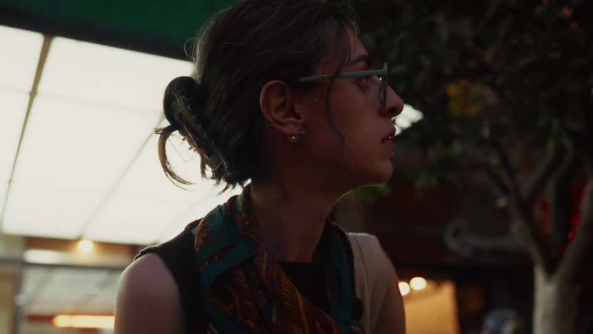 A young woman wearing glasses and a scarf observes her surroundings on a city street at night