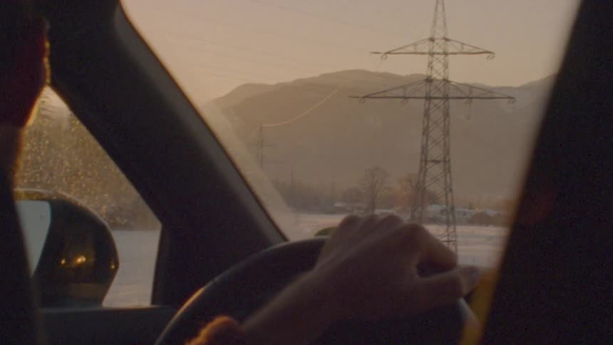 A point-of-view shot from a car driving through a snowy mountain landscape at sunset, with vintage film burn effects at the end