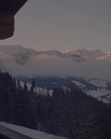 A slow pan across a majestic snow-covered mountain range and a forested valley filled with low-hanging clouds at sunrise