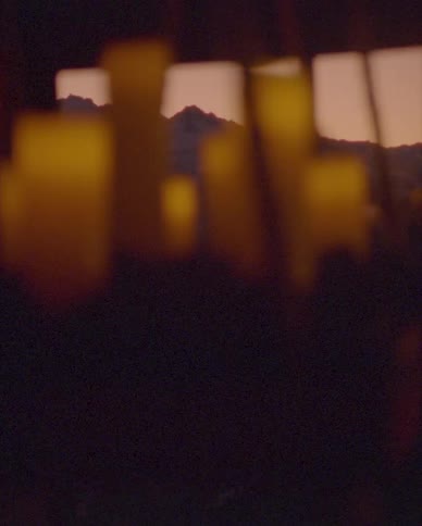 Out-of-focus candles cast a warm, ambient glow in a dark room, with a snowy mountain range visible at dusk through a window