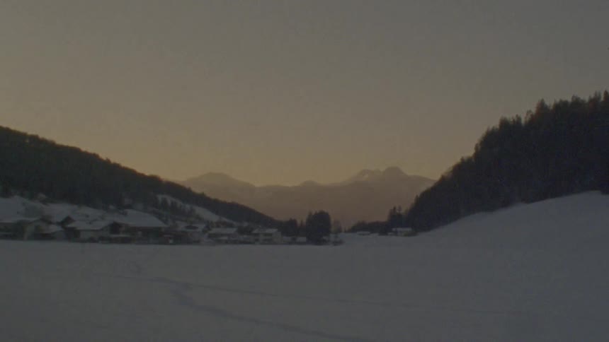 A point-of-view shot from a moving vehicle captures a serene, snow-covered mountain valley at sunrise