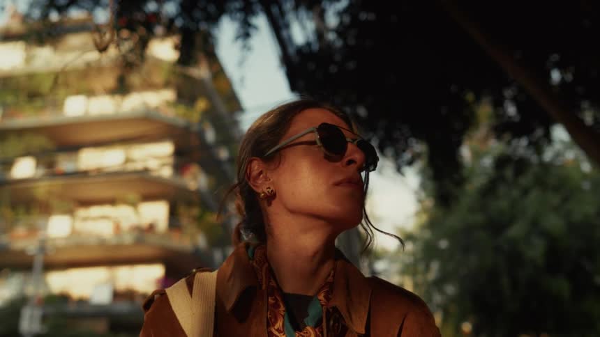 A stylish woman puts on sunglasses in slow motion on a sun-drenched city street before walking away