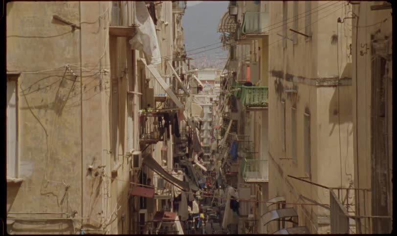 A slow zoom down a narrow, sunlit alley between weathered residential buildings in Naples, Italy