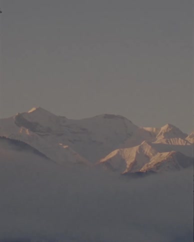 A panning shot reveals a beautiful snow-covered mountain range peeking through a layer of dense fog