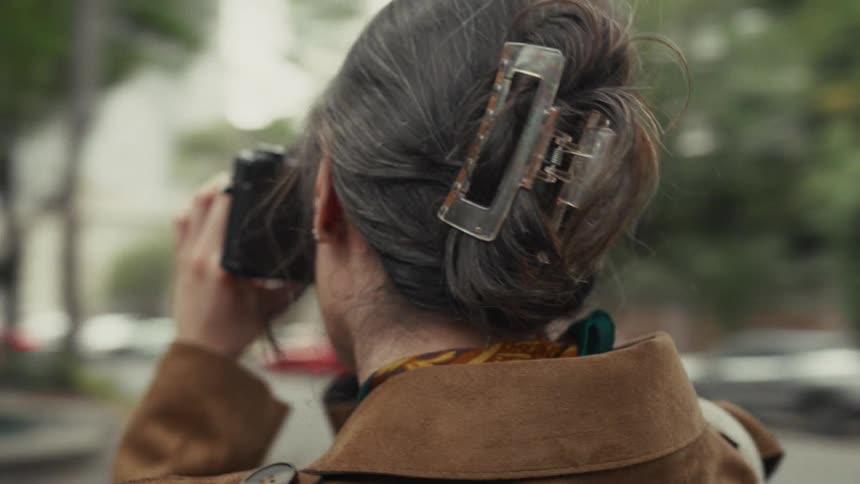 A female photographer is filmed in a dynamic orbit shot as she takes pictures with her camera on a bustling city street