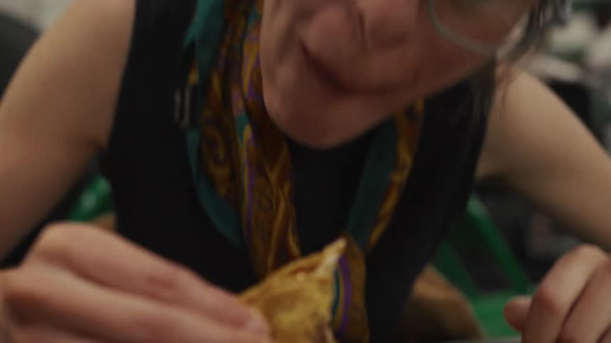 A hungry woman with glasses takes a large, satisfying bite of a taco in extreme slow motion