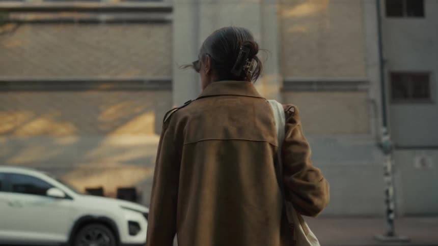 A fashionable young woman in sunglasses strolls along an urban sidewalk in slow motion during golden hour