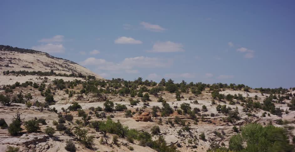 A scenic drive past the rugged, sandy hills and sparse greenery of the Utah desert on a bright, sunny day