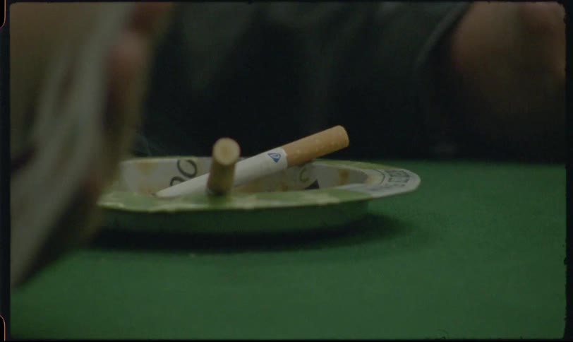 Vintage 8mm footage shows a close-up of a smoking cigarette in an ashtray on a green felt poker table