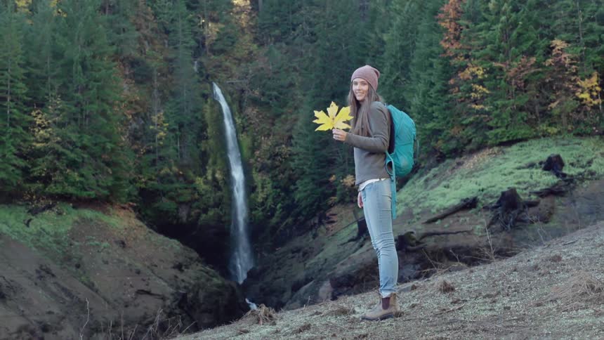 A woman is holding a large leaf in her hand by a cliff