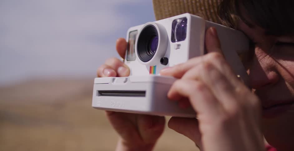 Close up of a smiling woman in a sun hat taking a photo with an instant camera in a beautiful sunlit field