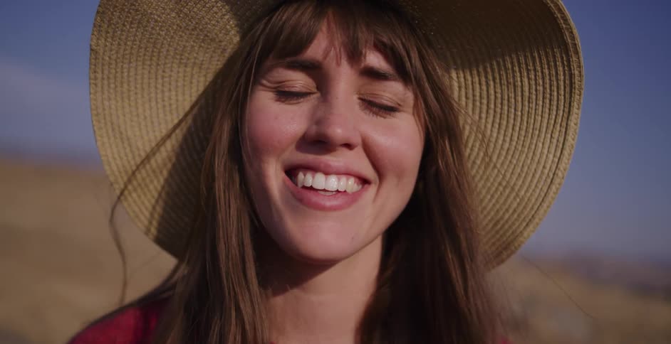 Close-up slow motion shot of a happy young woman in a sun hat smiling at the camera on a sunny day