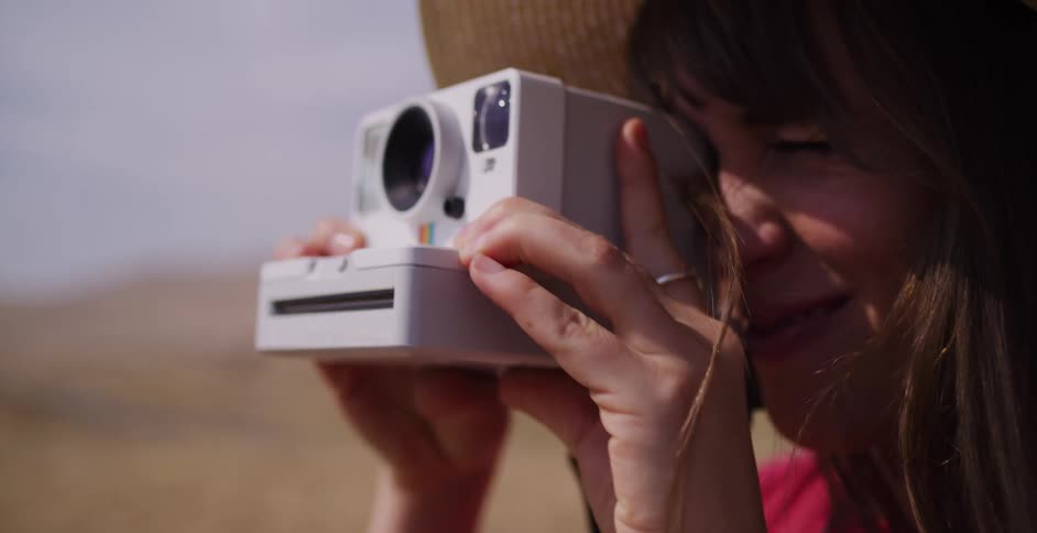 A happy woman in a straw sun hat takes a photo with a vintage-style instant camera in slow motion