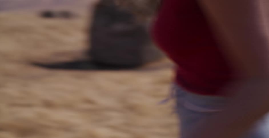 A carefree young woman laughs and runs through a sunny desert landscape while putting on her wide-brimmed hat