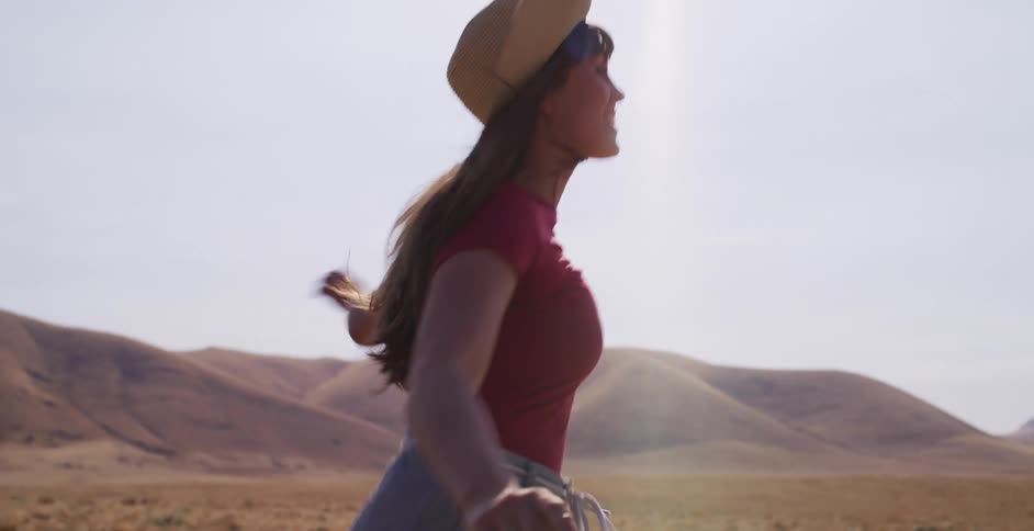 A carefree woman in a straw hat runs joyfully in slow motion through a vast, golden field under the bright sun