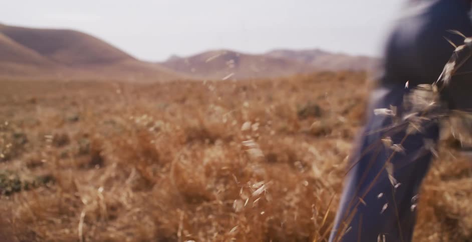 A person runs through a sun-drenched field of golden grass swaying in the wind