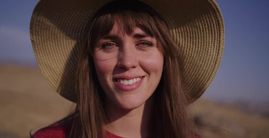 A beautiful young woman in a straw hat gives a warm and genuine smile to the camera on a sunny day outdoors