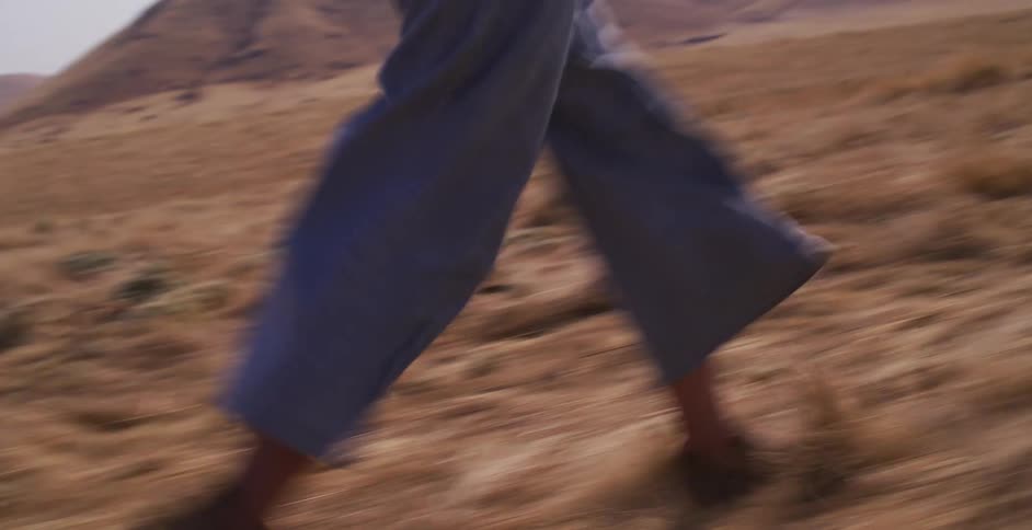 Cinematic slow motion shot follows a determined woman as she runs through a vast, arid landscape on a sunny day