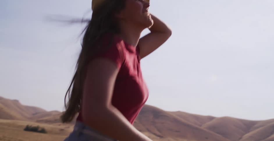 Slow motion side view of a carefree young woman in a straw hat running happily through a vast, dry field