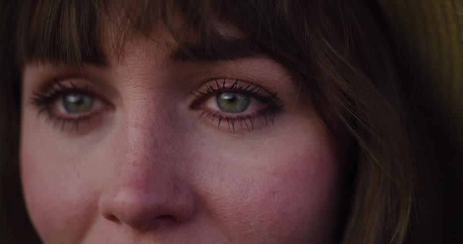 A dramatic close-up of a young brunette woman's green eyes welling up with tears