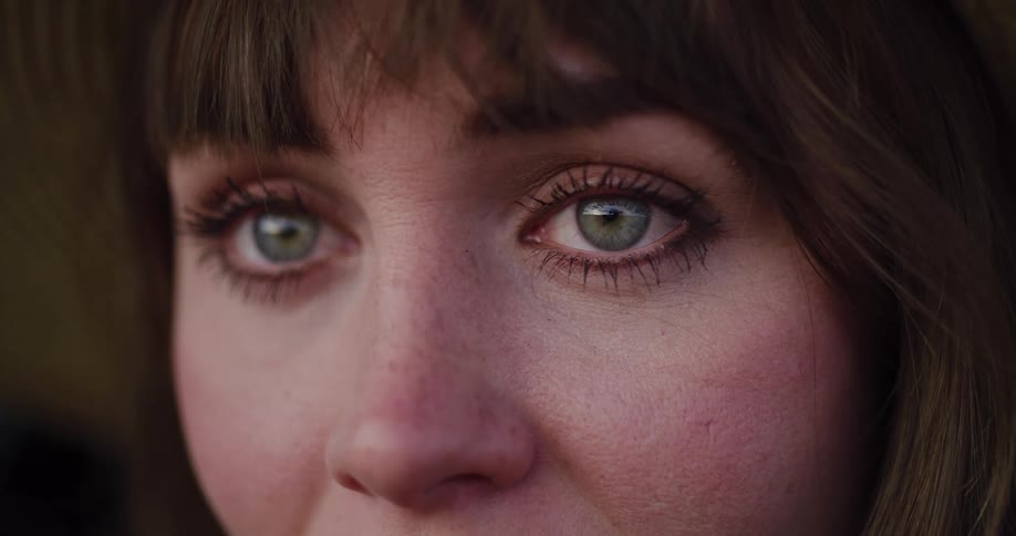 A poignant extreme close-up of a young woman's green eyes welling up with tears as she looks away