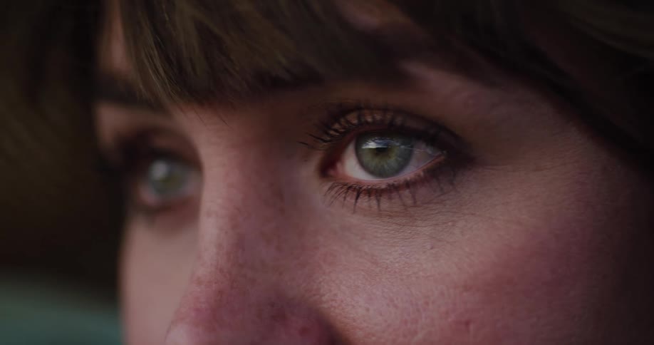 An intimate macro close-up of a thoughtful woman's beautiful green eyes blinking slowly in soft lighting