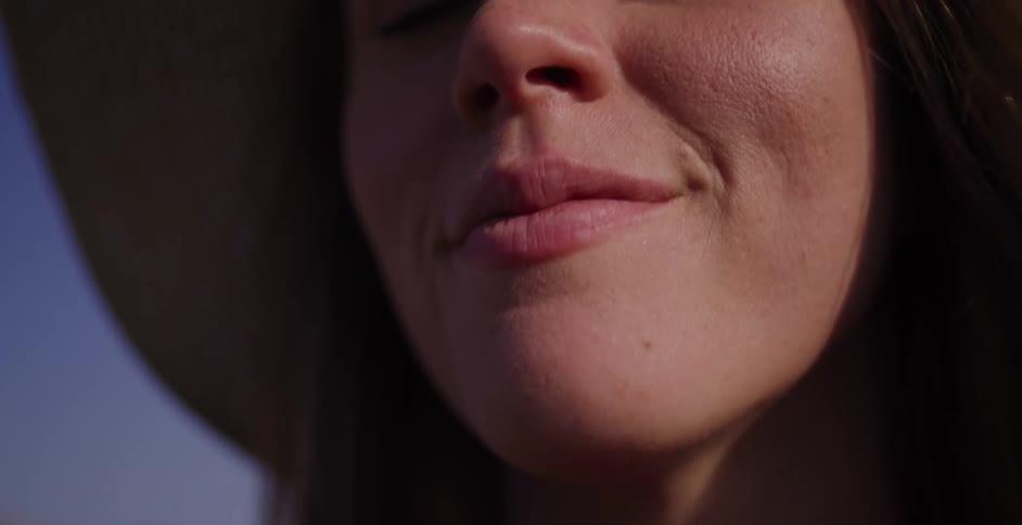 An extreme close-up shot in slow motion shows a serene woman in a straw hat closing her eyes to bask in the warm sunshine
