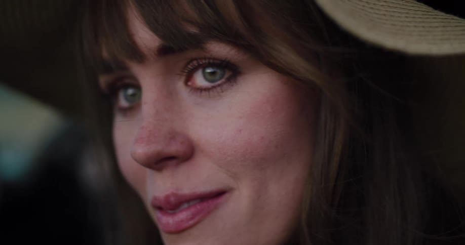 A beautiful woman with green eyes and a sun hat gazes thoughtfully in a cinematic close-up