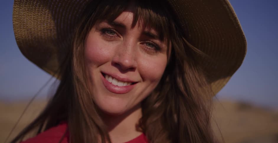 A slow-motion close-up of a beautiful young woman in a straw hat whose bright smile slowly fades into a sad expression