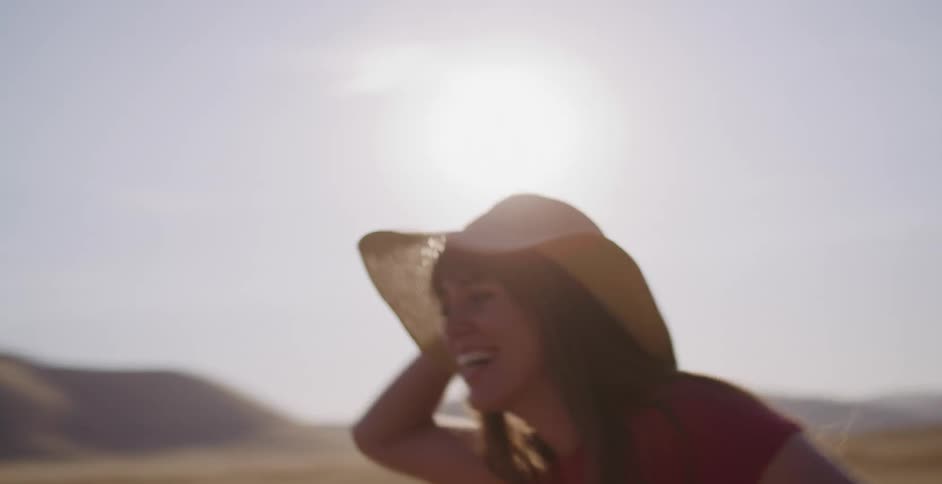 A smiling young woman in a straw hat runs joyfully through a sun-drenched desert landscape