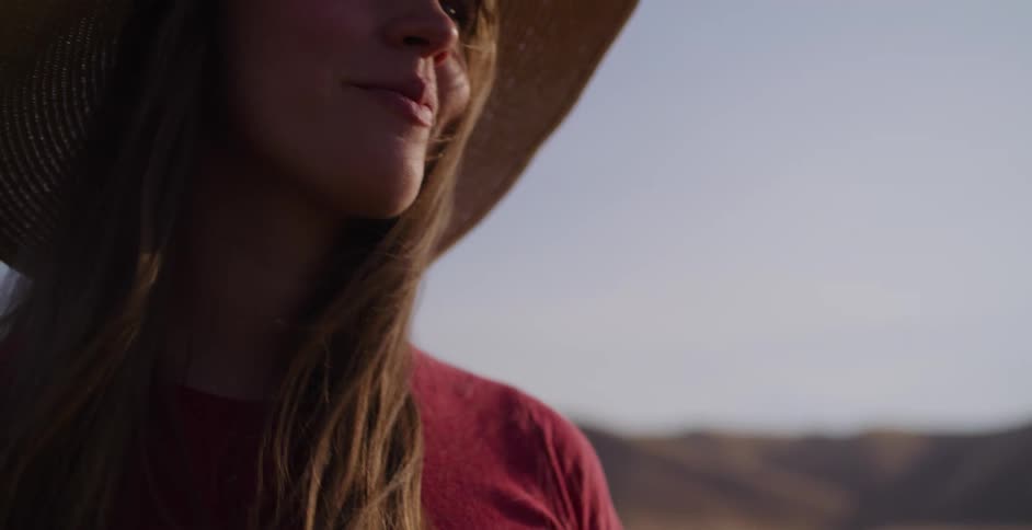 A close-up of a smiling young woman in a sun hat enjoying the warm glow of the golden hour outdoors