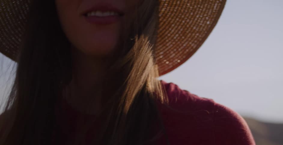 In slow motion, a smiling young woman in a floppy straw hat enjoys the warm golden hour light