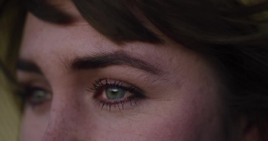 Extreme close-up on the green eyes of a pensive woman with wind blowing through her hair