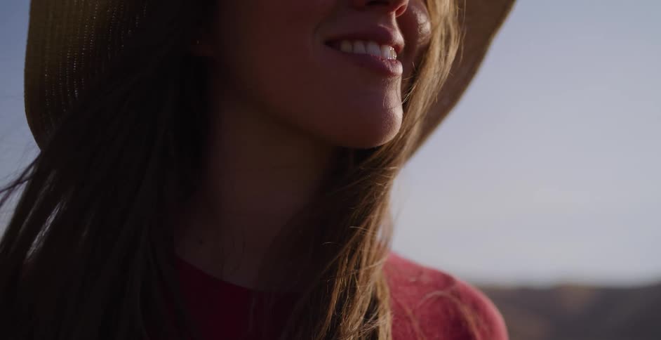 Slow motion close-up of a beautiful woman in a straw hat smiling while enjoying the outdoors at golden hour