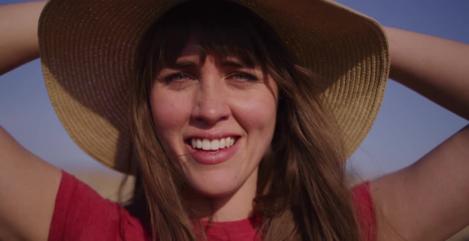 A beautiful, happy woman in a straw sun hat smiles into the camera in slow motion on a bright, sunny day