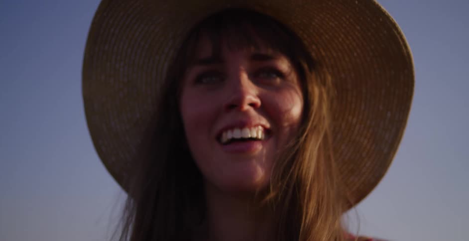 A smiling young woman in a straw hat lifts up an instant camera to take a picture during the golden hour