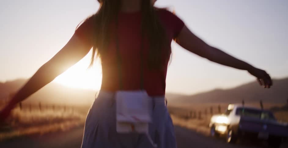 A happy young woman in a sun hat walks carefree down a country road at golden hour