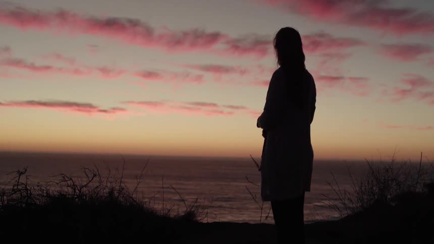 A woman looks out to sea at sunset